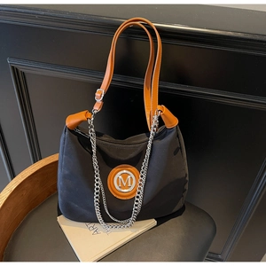 Detail of nylon tote bag with orange leather handles and silver chain on black chair