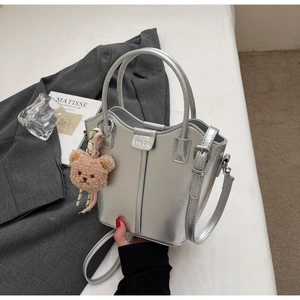 Detailed view of a silver bucket bag with plush bear charm and metallic finish