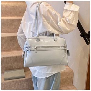 Close-up of light blue patent leather handbag with silver metal zippers and belt details
