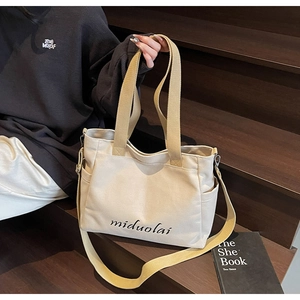 Detail of off-white canvas tote bag with adjustable shoulder strap and side pocket