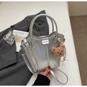 Detail of silver metallic bucket bag with a cute brown plush bear charm on white background