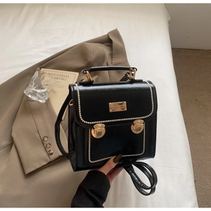 Detail of black glossy faux leather backpack with pearl straps and gold buckles