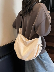 Minimalist beige crossbody dumpling bag with drawstring details shown on a model