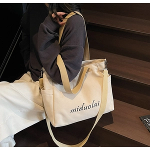 Detail view of off-white canvas tote bag featuring side pockets and black miduolai text