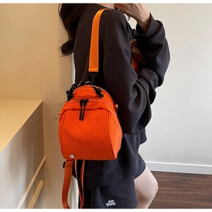Detail of a bright orange waterproof mini backpack with black and white woven handles