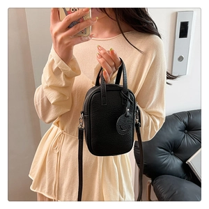 Close-up of black lychee-grain leather mini crossbody bag with top handle and round charm