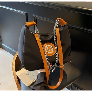 Detail of black nylon crescent bag with silver M logo and brown leather strap on chair