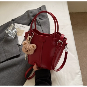 Detail view of red glossy patent leather bucket bag with plush bear charm and crossbody strap