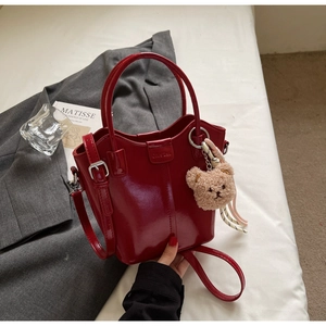 Close-up of red patent leather bucket bag with shiny finish and teddy bear charm