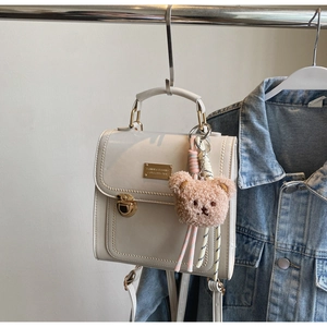 Dettaglio borsa bianca in pelle con fibbia dorata e ciondolo a forma di orsetto marrone