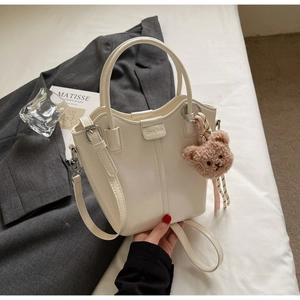 Detail of cream bucket bag with vertical stitching and cute plush bear charm accessory