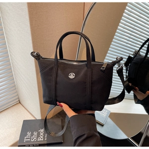 Detailed macro view of the black nylon bag with a circular M logo and detachable strap