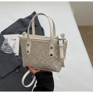 Detail of cream bucket bag showing geometric floral weave and metallic rivet accents