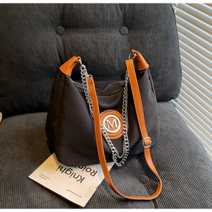 Detail of canvas crossbody bag featuring orange leather strap and metallic M logo