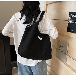 Detail of black tote bag with 3D dot texture and woven label on a person shoulder
