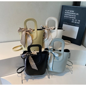 Dettaglio di quattro borse a secchiello grana litchi con manici vuoti e foulard di seta
