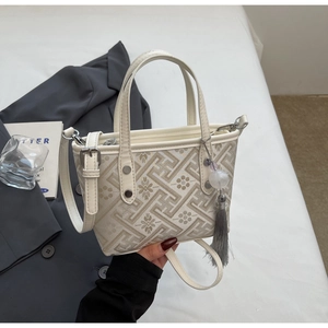 Detailed view of the beige embroidered bucket bag with patterns and tassel accessory