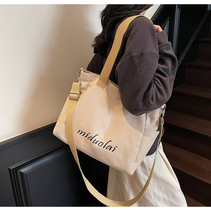 Detail of beige canvas tote bag with black cursive script and adjustable crossbody strap