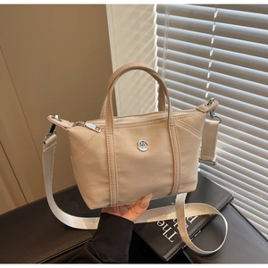 Detail of beige canvas crossbody bag with wide shoulder strap and silver M FASHION logo