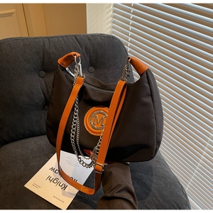 Detail of black canvas bag with orange leather handles and silver metal chain strap