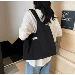 Detail of black polka dot canvas tote bag showing textured fabric and brand label on strap
