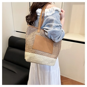 Detail of a dual-tone woven straw tote bag with brown leather patch and slim shoulder straps