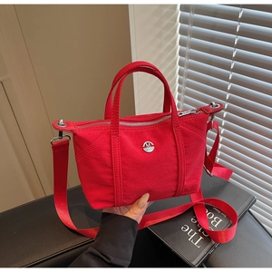 Detailed shot of a red canvas crossbody bag with silver logo and woven shoulder strap