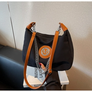Close-up of black canvas tote bag with brown leather handles and metal M logo detail