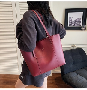 Vue d'épaule d'un cabas en cuir bordeaux avec lettrage doré porté par un mannequin chic