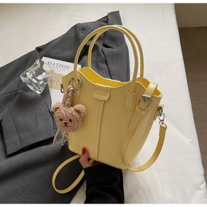 Detail of yellow bucket bag with smooth PU leather texture and plush bear pendant