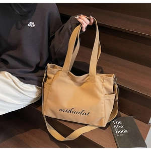Detail of khaki canvas tote with miduolai script and side pocket on wooden stairs