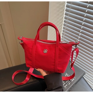 Close-up of red canvas bag with round metal M logo and silver zipper on dark background