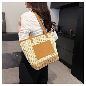 Detailed shot of a large straw tote bag featuring brown leather trim and woven texture