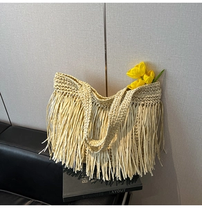 Gros plan du sac fourre-tout en paille beige à franges sur un banc avec des fleurs