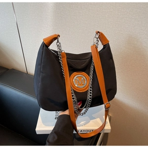 Detail of metal M logo on black nylon bag with brown leather trim and chain strap