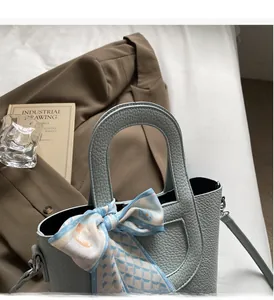Dettaglio della borsa in pelle azzurra con manico decorato da un foulard di seta a quadri