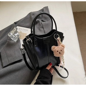 Detail of black glossy bucket bag with cute plush bear charm and silver hardware