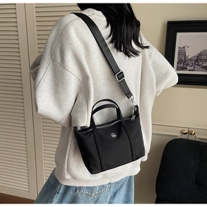 Side view of black canvas crossbody bag with metal logo on casual grey sweatshirt