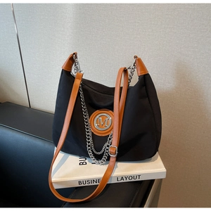 Detail of black nylon dumpling bag with brown leather trim and silver M logo on a book