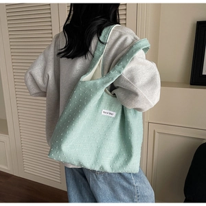 Detail shot of mint green textured canvas tote bag with woven brand label on model