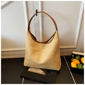 Detail view of woven straw tote bag with brown leather handles and brand logo texture