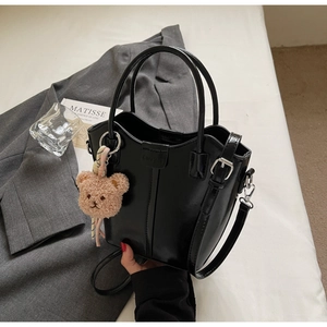 Glossy black bucket bag with a cute plush bear charm and adjustable shoulder strap