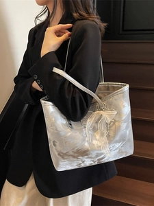 Silberne Metallic-Tote-Bag mit Wellenstruktur und weißer Schleife am Modell getragen