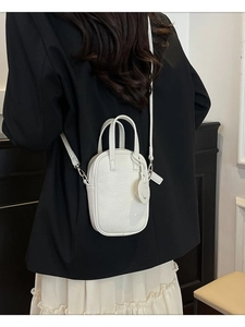 White pebbled leather crossbody bag shown on a model in a black blazer and white skirt