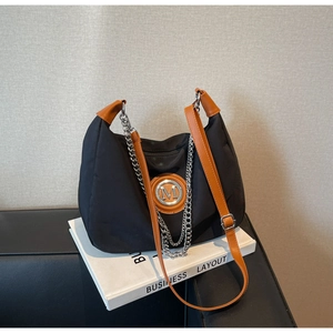 Detail of black canvas dumpling bag with brown leather trim and metallic M logo