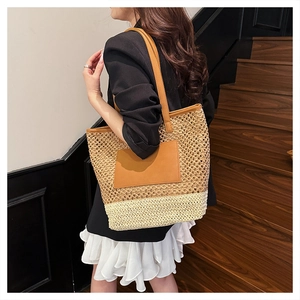 Close-up of large straw tote bag with brown leather handles and two-tone woven texture