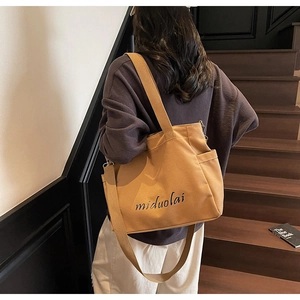 Detail of a large mustard yellow canvas tote bag featuring miduolai embroidery on a shoulder strap