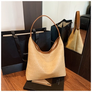 Detailed view of woven straw tote bag with brown leather strap on wooden surface