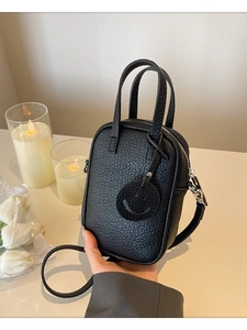 Black litchi grain leather crossbody bag with dual handles and smiley face charm