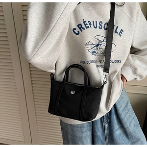 Close-up of a black nylon crossbody bag with silver hardware on a casual model outfit